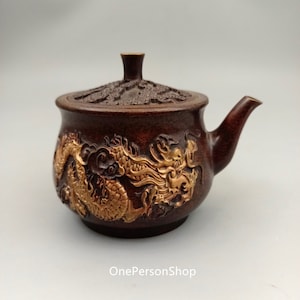 May include: A small, brown teapot with a lid and a gold dragon design. The teapot has a spout and a handle.