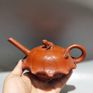 May include: A terracotta teapot with a frog on the lid. The teapot has a detailed design of a lotus flower on the body.