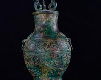 May include: A green bronze Chinese vase with intricate carvings and a lid with two handles. The vase has a round body and a narrow neck.