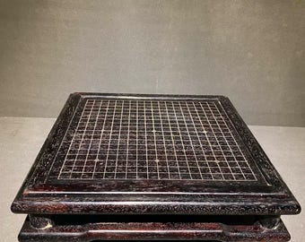 May include: A dark brown wooden Go board with a grid pattern. The board is rectangular with rounded corners and rests on four short, rounded legs. The wood grain is visible, adding texture to the surface.