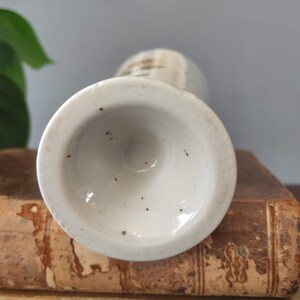 May include: The bottom of a white ceramic vase with a brown speckled glaze. The vase has a round base and a slightly flared opening.