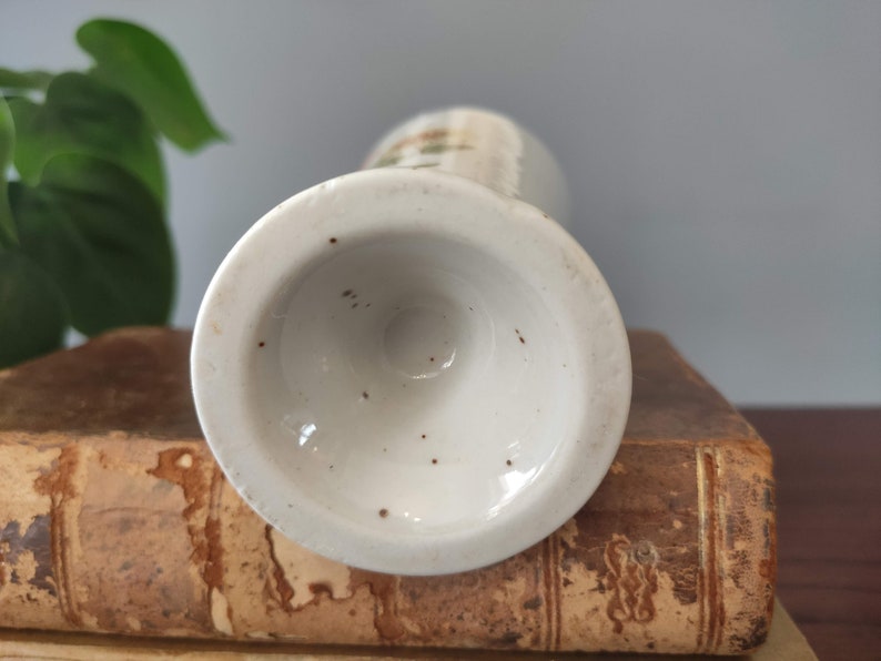 May include: The bottom of a white ceramic vase with a brown speckled glaze. The vase has a round base and a slightly flared opening.
