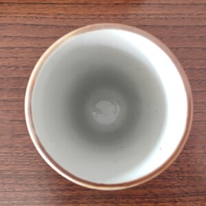May include: A white ceramic cup with a brown rim. The cup is empty and sitting on a wooden surface.