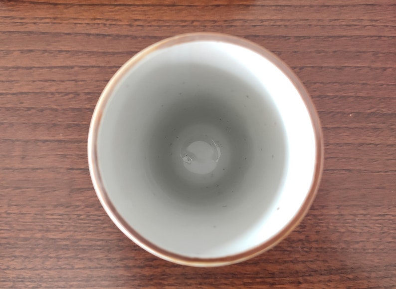 May include: A white ceramic cup with a brown rim. The cup is empty and sitting on a wooden surface.