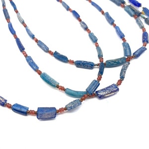 Peut inclure: Un collier compos&eacute; de perles de verre bleues et roses. Les perles sont cylindriques et ont une surface textur&eacute;e. Le collier est superpos&eacute; et a un aspect vintage.