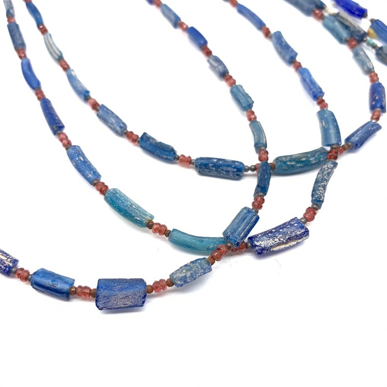 Peut inclure: Un collier compos&eacute; de perles de verre bleues et roses. Les perles sont cylindriques et ont une surface textur&eacute;e. Le collier est superpos&eacute; et a un aspect vintage.