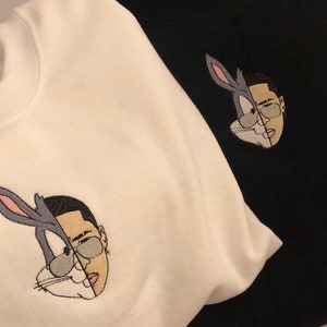 May include: Two white and black sweatshirts with an embroidered image of Bugs Bunny and a man's face. The image is split down the middle, with Bugs Bunny on the left and the man's face on the right.