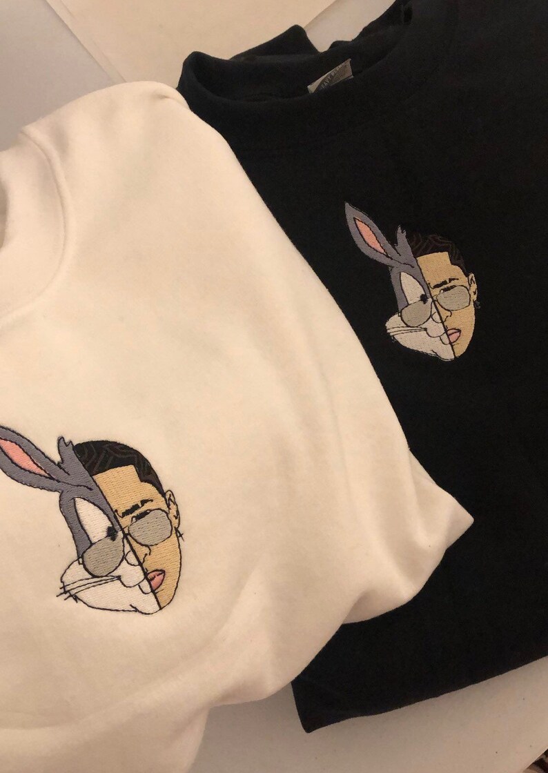 May include: Two white and black sweatshirts with an embroidered image of Bugs Bunny and a man's face. The image is split down the middle, with Bugs Bunny on the left and the man's face on the right.