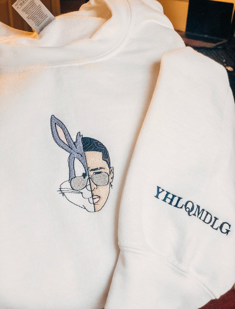 May include: White sweatshirt with an embroidered image of Bugs Bunny and a man's face. The sleeve has the text "YHLQMDLG" embroidered in black.