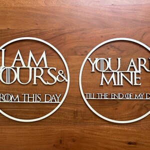 Może przedstawiać: Dwa białe, okrągłe elementy dekoracji ściennej z napisami "I AM YOURS & FROM THIS DAY" i "YOU ARE MINE TILL THE END OF MY DAYS" w stylizowanej czcionce. Grafika jest umieszczona na drewnianym tle.