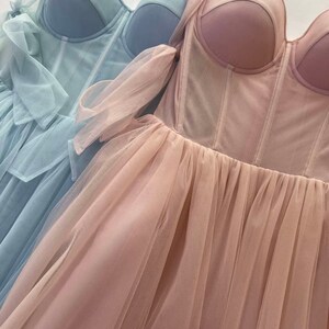 May include: Two tulle dresses with a corset bodice. One dress is light blue and the other is blush pink.