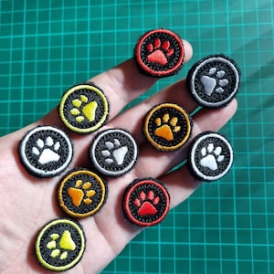 May include: Assortment of 10 paw print themed controller caps in various colours, including red, orange, yellow, white, and grey. The caps are circular and feature a black outline with a paw print in the centre.