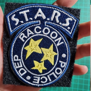 May include: A blue and white embroidered patch with the text "S.T.A.R.S. RACOON POLICE. DEP" and three yellow stars.