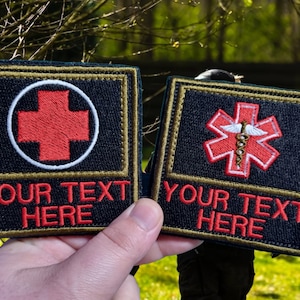 May include: Two black and gold embroidered patches with red medical symbols. The left patch has a red cross in a white circle and the text "YOUR TEXT HERE". The right patch has a red star of life with a white snake and wings and the text "YOUR TEXT HERE".