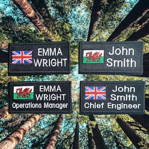 May include: Four black name tags with embroidered text and flags. The top left tag reads "Emma Wright" with a Union Jack flag. The top right tag reads "John Smith" with a Welsh flag. The bottom left tag reads "Emma Wright Operations Manager" with a Welsh flag. The bottom right tag reads "John Smith Chief Engineer" with a Union Jack flag.