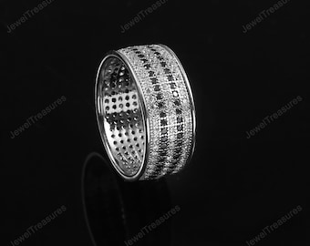 May include: A silver ring with a band design featuring alternating rows of white and black stones. The ring is set against a black background, highlighting its reflective surface and intricate details. The ring is a piece of jewelry.