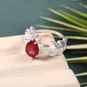 Könnte beinhalten: Ein silberner Ring mit einem roten Edelstein, der in einem Blattdesign gefasst ist.