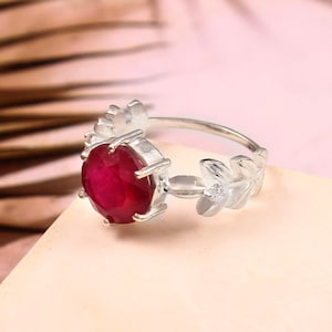 Pode incluir: Um anel de prata com uma grande gema de rubi oval e um design de folhas na banda.