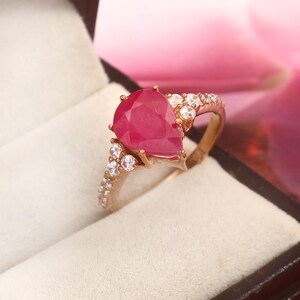 May include: A pear-shaped ruby ring set in rose gold with a band of small white diamonds.