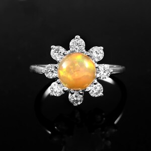 May include: A silver ring with a round opal gemstone surrounded by smaller clear gemstones in a flower shape.