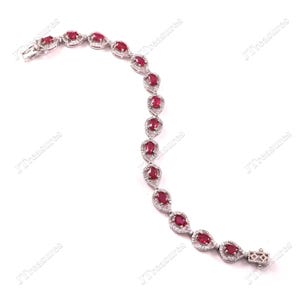 May include: A silver-toned bracelet featuring a series of oval-shaped red rubies, each surrounded by a halo of small white stones. The links are connected in a curved, flexible design, ending with a rectangular clasp mechanism at one end.