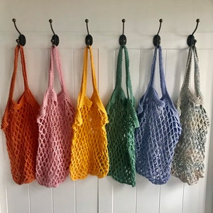Può includere: Sei borse in rete all'uncinetto appese a ganci. Le borse sono di vari colori, tra cui arancione, rosa, giallo, verde, blu e grigio.