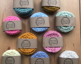 May include: Ten round, crocheted, reusable face scrubbies in various colors, including light blue, pink, yellow, and beige. Each scrubbie has a brown paper label with the text "Hand crocheted 100% cotton Face Scrubbies".