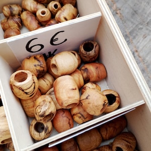 Könnte beinhalten: Holzperlen in verschiedenen Formen und Größen, präsentiert in einer unterteilten Holzkiste. Die Perlen haben natürliche Holztöne mit sichtbaren Maserungsmustern. Einige Perlen sind zylindrisch, andere runder, alle mit einem Loch.