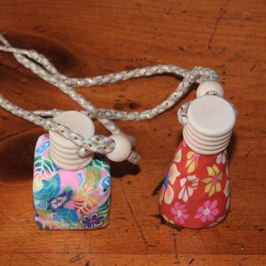 May include: Two small, colourful, floral patterned bottles with wooden stoppers and a gold cord. The bottles are hanging from the cord.