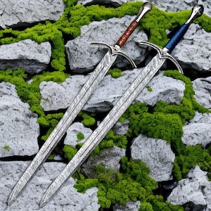 Puede incluir: Dos espadas largas con hojas de acero damasco estampado y guardas plateadas. Una espada tiene una empuñadura envuelta en cuero marrón, mientras que la otra tiene una empuñadura envuelta en cuero azul con una pequeña piedra azul en la guarda.