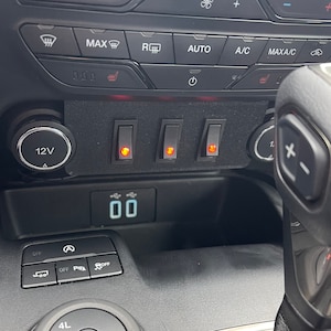 May include: A black dashboard with a 12V outlet, three toggle switches, and a digital display reading "00".