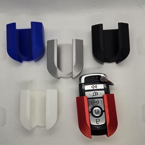 May include: Five key fob holders in different colors: blue, silver, black, white, and red. The red holder is holding a car key fob with buttons.