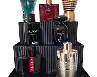 May include: A black three-tiered stand with a ribbed design holds a collection of perfume bottles. The bottles are various shapes and sizes, with a mix of colors including gold, silver, blue, red, and black. The bottles have labels with brand names such as "Sauvage", "Dior", "Prada", "Versace", and "Night de Paris".
