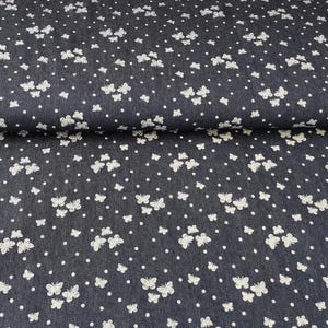 Può includere: Un tessuto di jeans blu scuro con un motivo a pois bianchi e una stampa di farfalle bianche.