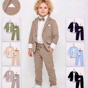 May include: A young boy in a tan suit, white shirt, and bow tie. The suit comprises a blazer and trousers. Further suits in green, beige, grey, navy, light blue, and black are shown.