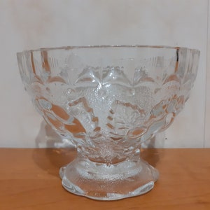 May include: A clear glass bowl with a decorative floral pattern. The bowl has a wide, round base and a flared rim.