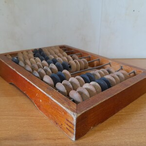 Può includere: Un abaco in legno con perline marroni e aste metalliche nere. L'abaco è in una cornice di legno con una finitura in legno naturale.