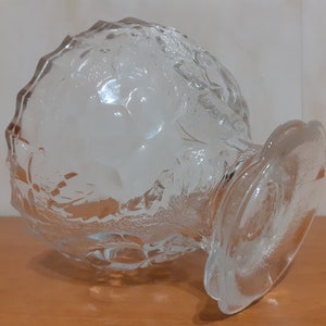 May include: A clear glass bowl with a textured surface and a wide base. The bowl is designed with a grape motif.
