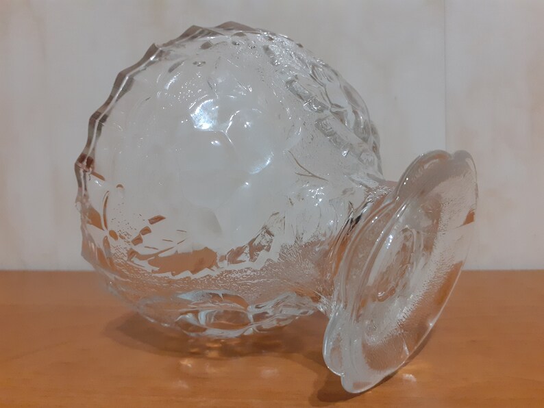 May include: A clear glass bowl with a textured surface and a wide base. The bowl is designed with a grape motif.
