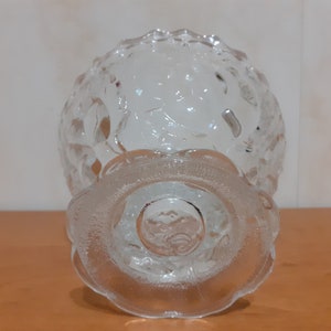 May include: A clear glass bowl with a textured design and a pedestal base. The bowl is empty and appears to be made of thick glass.