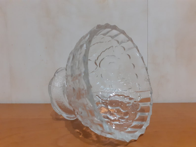 May include: A clear glass bowl with a textured surface. The bowl has a wide, round base and a deep, rounded bowl. The bowl is made of clear glass and has a textured surface.