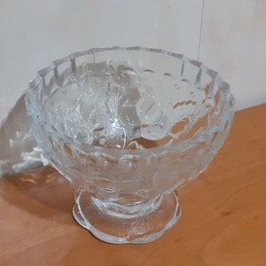 May include: A clear glass bowl with a pedestal base. The bowl has a decorative, embossed pattern of leaves and flowers.