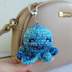 May include: A crocheted blue octopus keyring with a smiling face. The octopus has eight tentacles and is attached to a silver key ring.