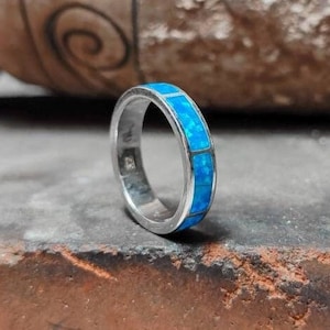 Peut inclure: Une bague en argent avec une incrustation d'opale bleue. La bague est posée sur une surface brune.