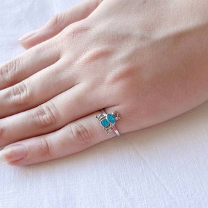 Puede incluir: Un anillo de plata con dos piedras turquesa engastadas en un delicado diseño de mariposa.