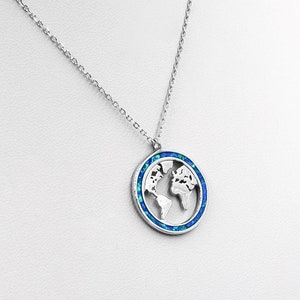 May include: Silver-toned necklace featuring a pendant with a world map design. The pendant has a blue and teal border and a cut-out of the continents. The necklace is displayed against a white background.