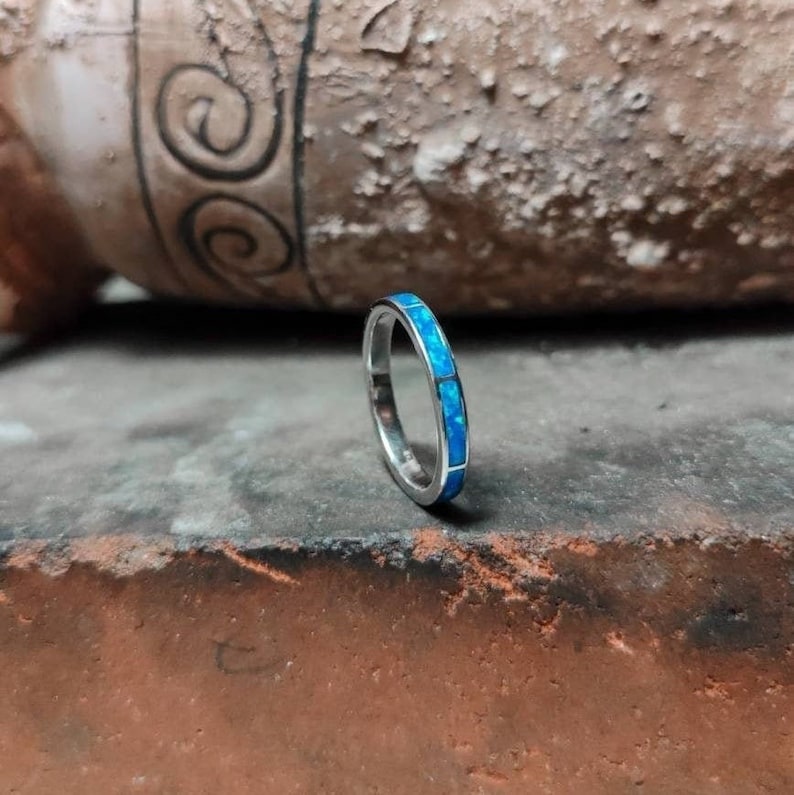 K&ouml;nnte beinhalten: Ein silberner Bandring mit einer Reihe von blauen Opal-Steinen.