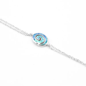 Puede incluir: Un brazalete de cadena de plata con un colgante de espiral de ópalo azul y verde.