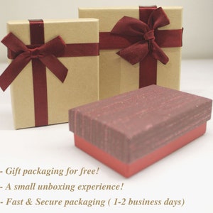 K&ouml;nnte beinhalten: Drei Geschenkboxen mit rotem Band und Schleifen. Die Boxen sind aus braunem Karton und haben eine strukturierte Oberfl&auml;che. Der Text auf dem Bild lautet: - Geschenkverpackung kostenlos! - Ein kleines Auspack-Erlebnis! - Schnelle und sichere Verpackung (1-2 Werktage)