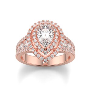 May include: Rose gold engagement ring featuring a pear-shaped center stone surrounded by a double halo of smaller diamonds. The band is also adorned with diamonds, creating a sparkling, elegant design. The ring is set against a white background.